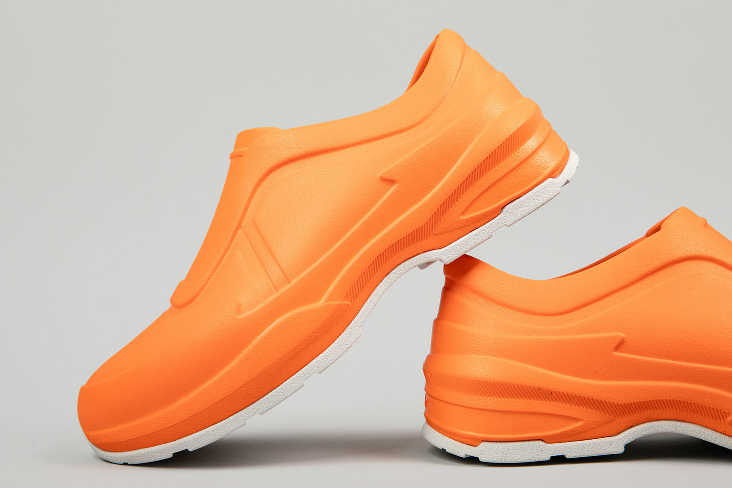 A close-up of vibrant orange STAND+ slip-resistant work shoes with a white sole, designed for medical professionals and those on their feet all day.