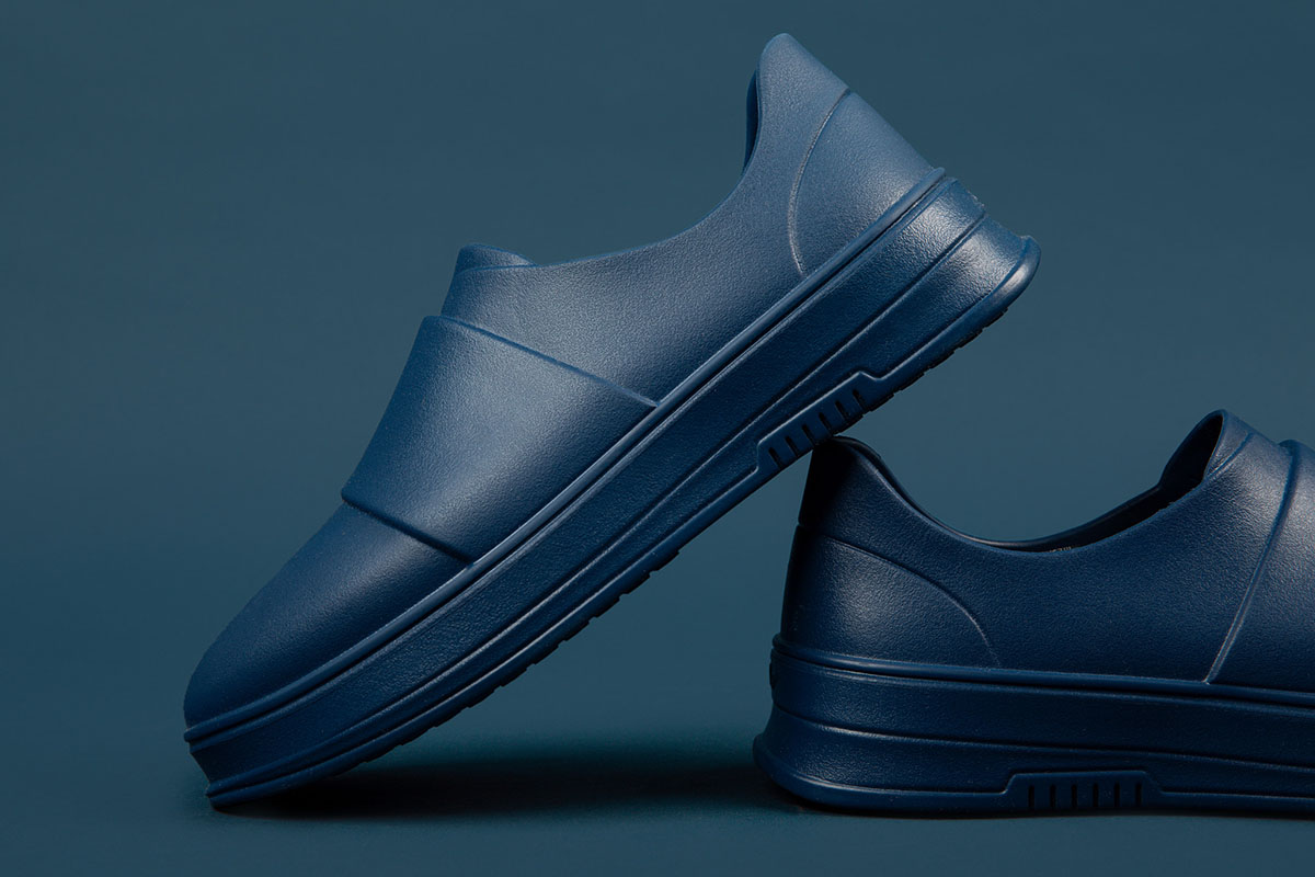 Navy blue slip-on shoes positioned against a dark blue background, with a sleek and modern appearance.