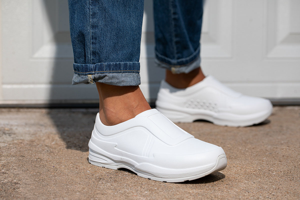 White slip-on shoes worn by a person standing on a textured concrete surface.
