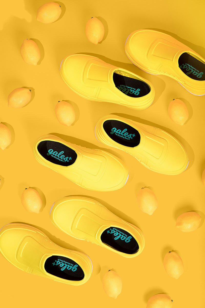 Bright yellow slip-on shoes arranged in a diagonal pattern on a textured yellow background, creating a vibrant visual effect.