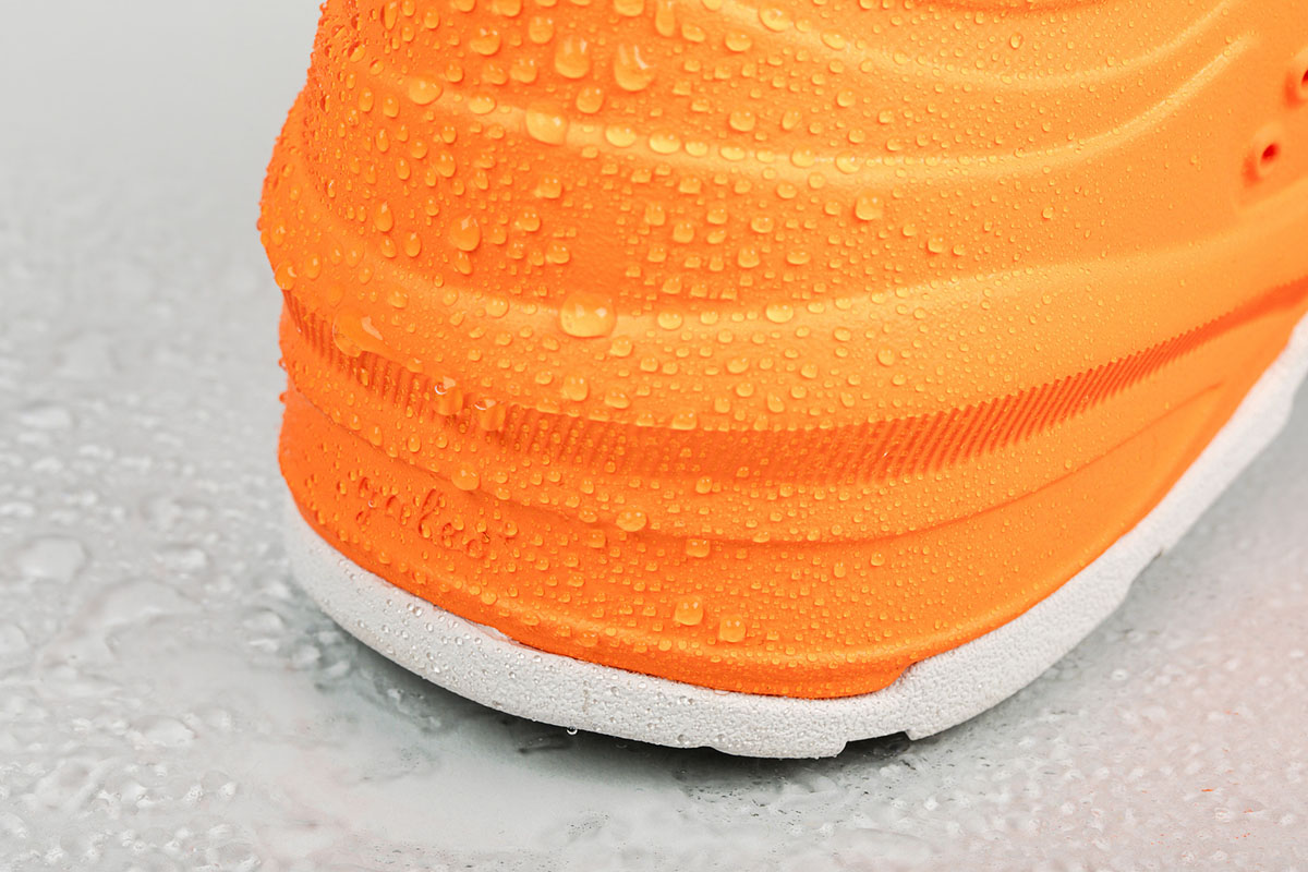 Close-up of an orange slip-on shoe covered in water droplets, highlighting its waterproof feature.